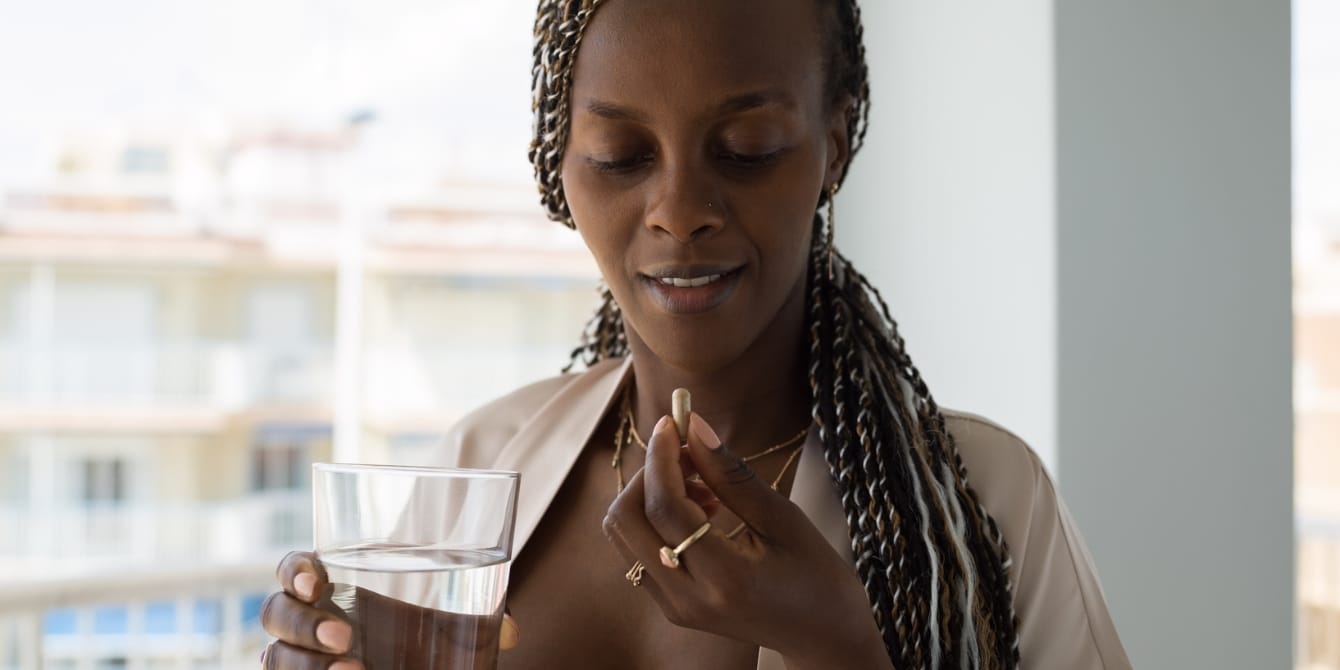 woman holding vitamin and water - best postnatal vitamins