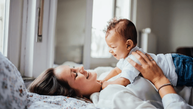 mom lying on her back, holding her infant on her stomach, learning how to stimulate baby brain development