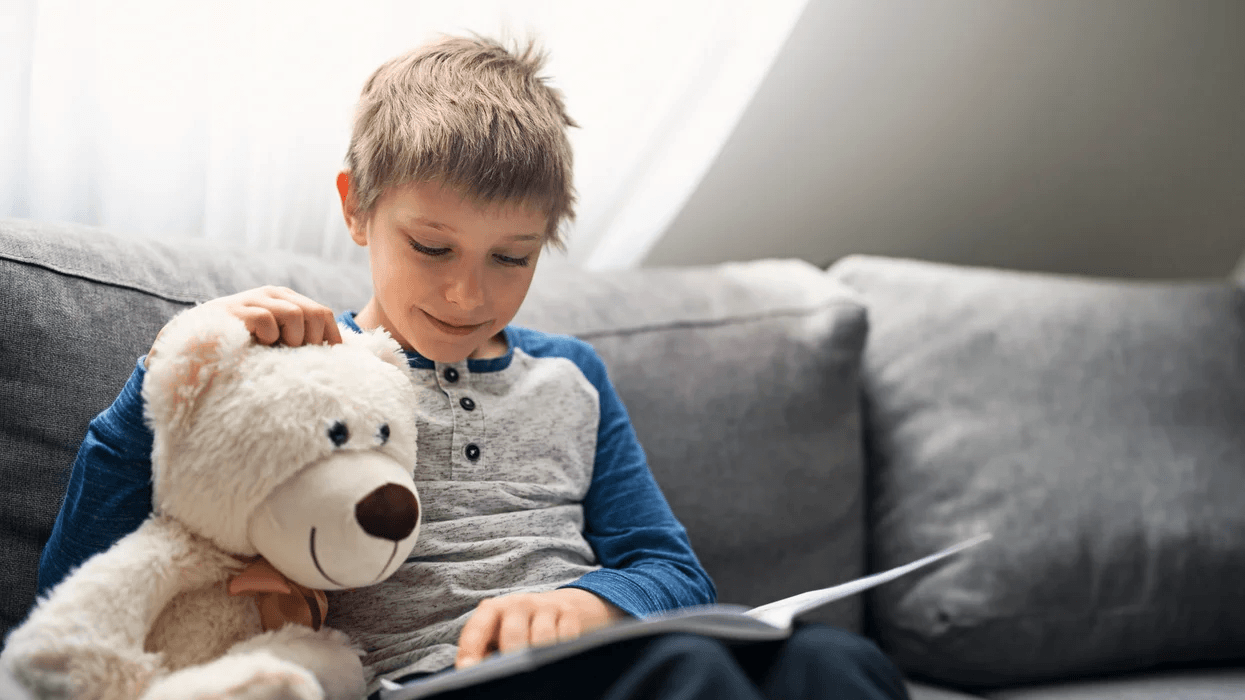 child reading a book holding a stuffed animal