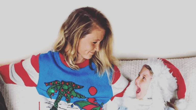 mom wearing christmas sweater smiling at child wearing santa hat- moms make christmas happen