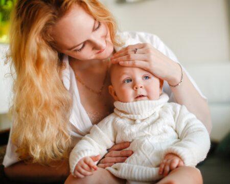 caring beautiful blonde mom with a baby in a sweater sitting on her lap mom touches the babys t20 YELaP1