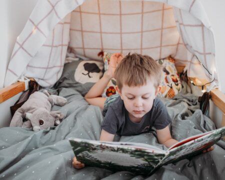 little boy reading book in his bed at home spending time at home during lockdown self isolation t20 KARGEX