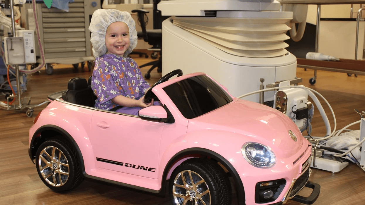 little girl in surgical gear in a toy car