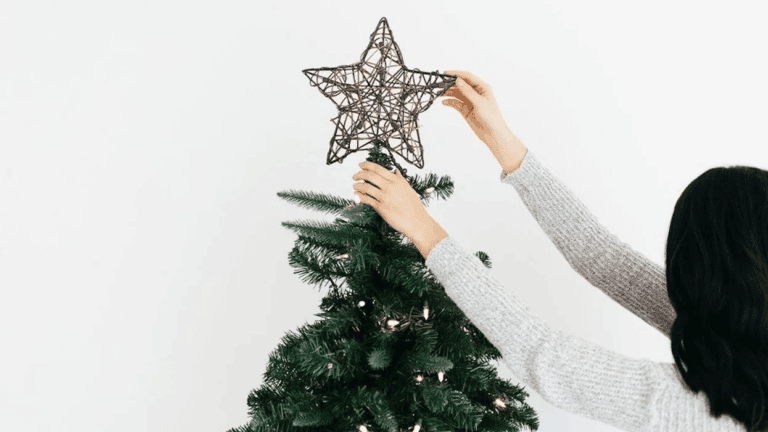 woman putting star on a Christmas tree- is it too early to decorate for christmas