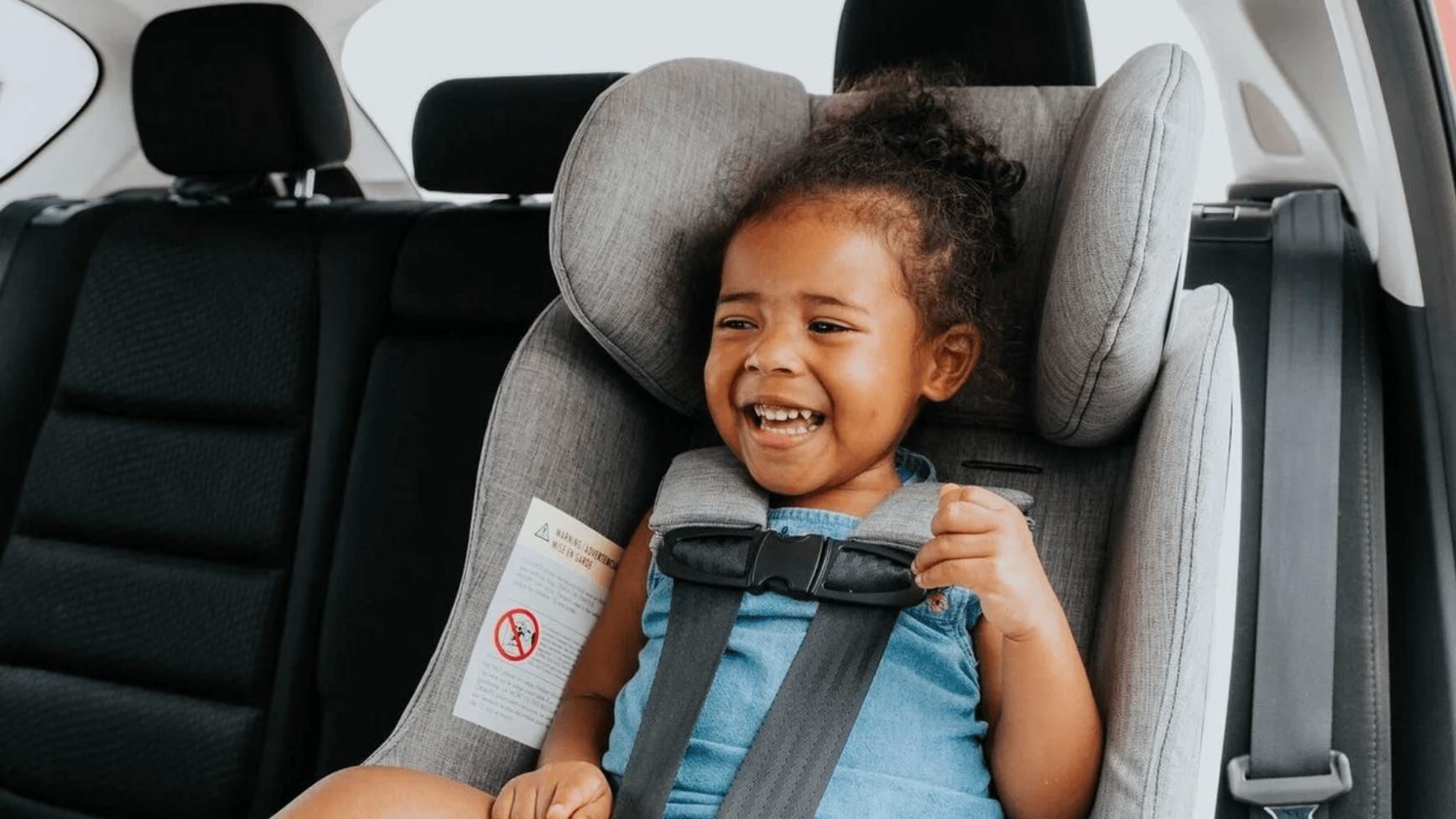 child sitting in a car seat laughing - transition from car seat to booster