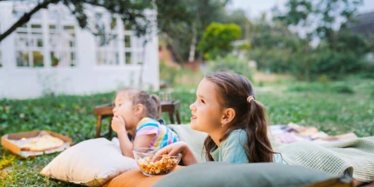 little girls watching a movie for outdoor movie night, a perfect summer activity- how to host an outdoor movie night