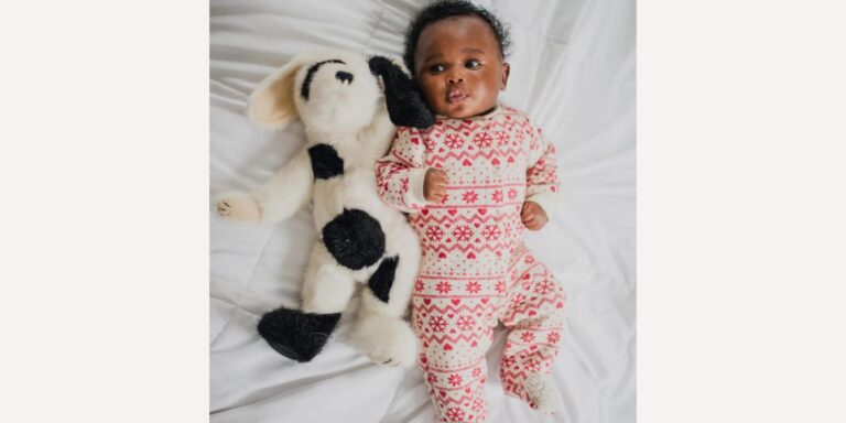 baby wearing fair isle onesie laying down with stuffed animal dog- aries names