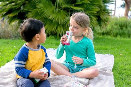 two kids sitting in the grass drinking juice boxes