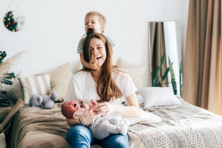 mom holding newborn while toddler plays with her hair