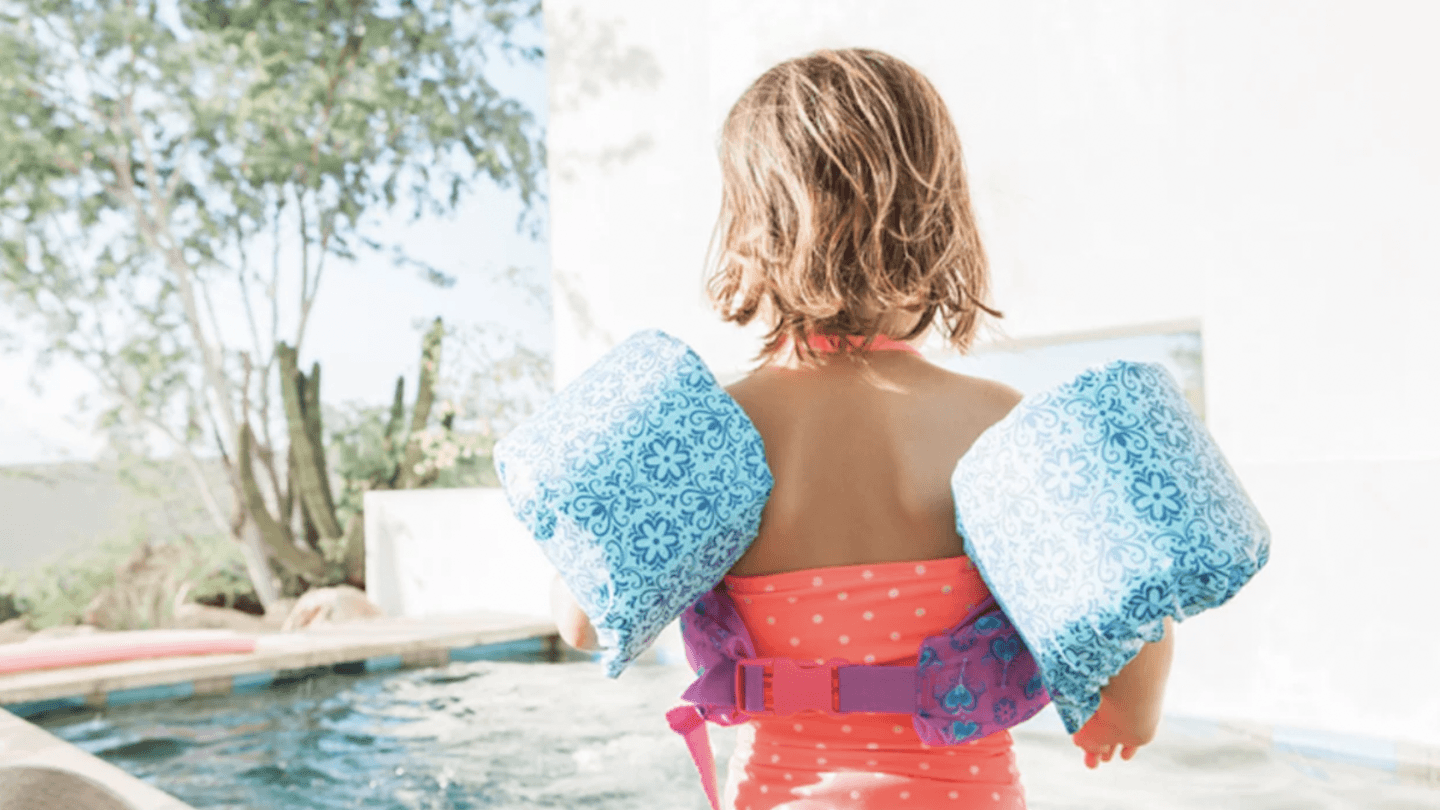 young girl standing outside a pool wearing floaties