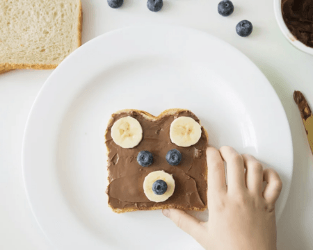 childs hand reaches for nutella toast with fruit