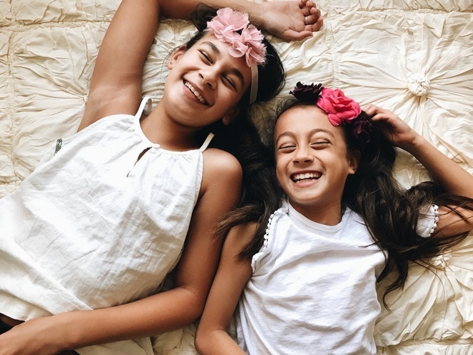 two girls wearing flower headbands lying down laughing- cultivating gratitude