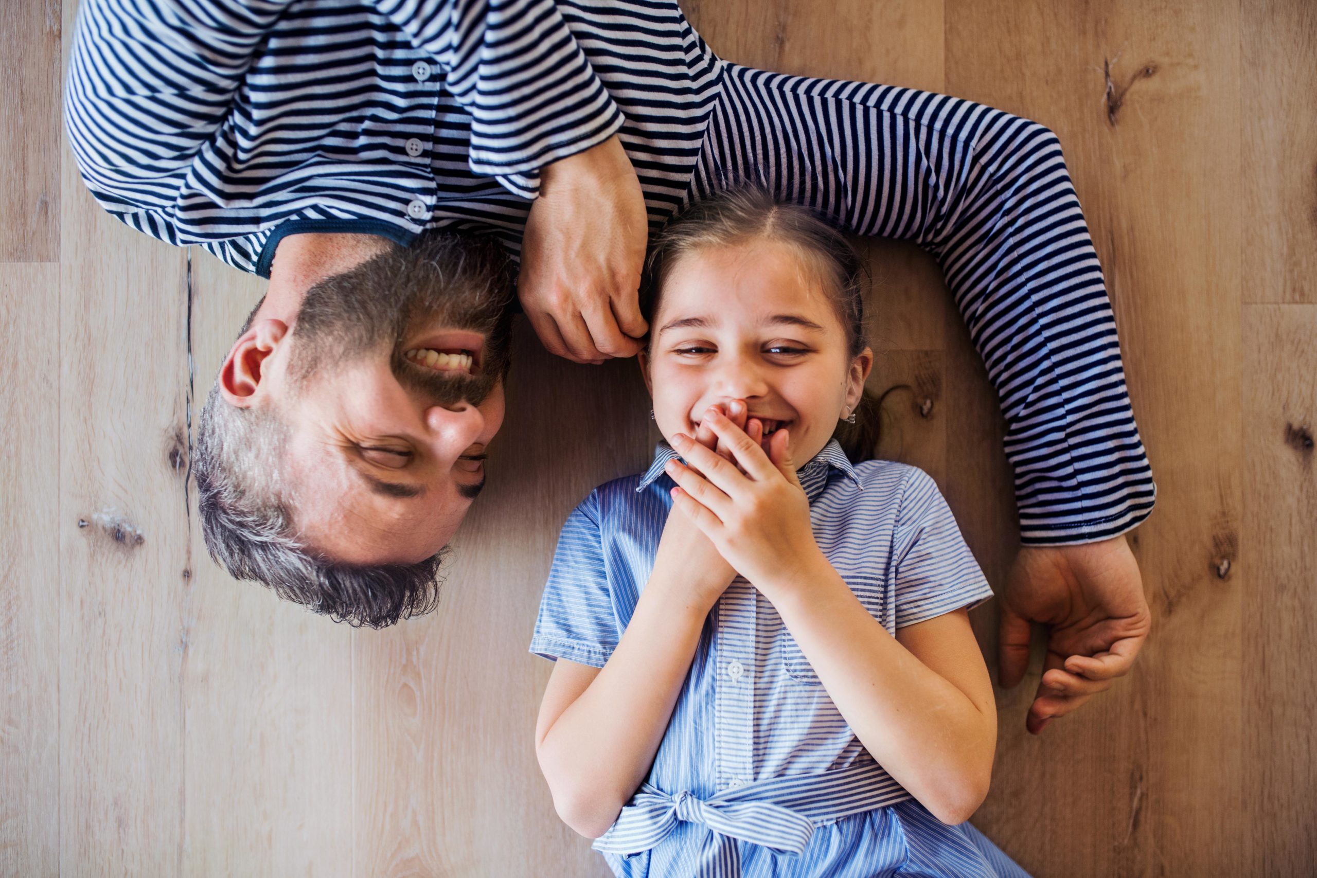 dad laughing with daughter laying on the floor