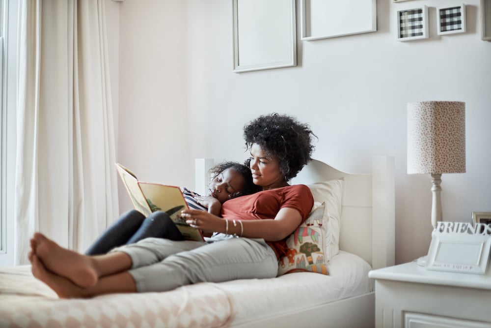 mom reading a book to her daughter in bed - keeping a consistent bedtime routine