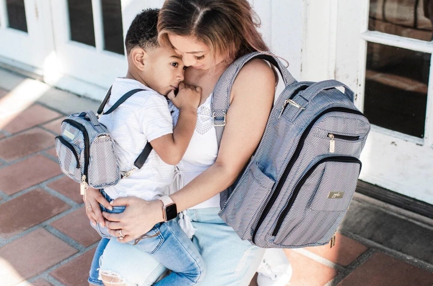 30 stylish diaper bags that don’t look like diaper bags mom holding a toddler while wearing a diaper bag