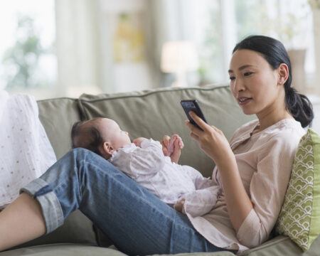 mom on her phone while holding a baby on her lap - baby feeding apps