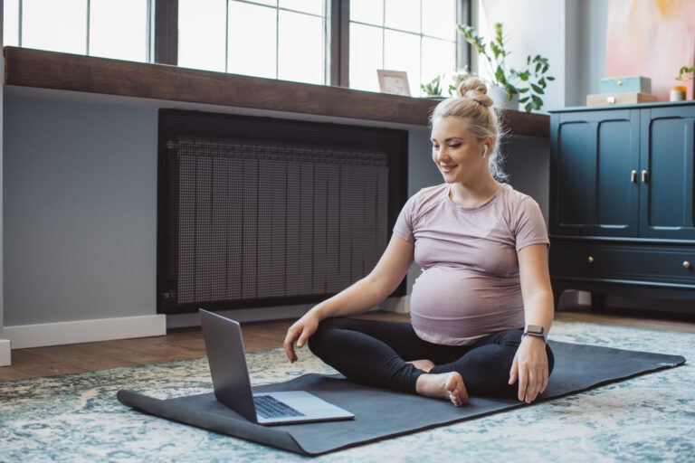 pregnant woman exercising with open laptop on yoga mat, learning how to prevent diastasis recti