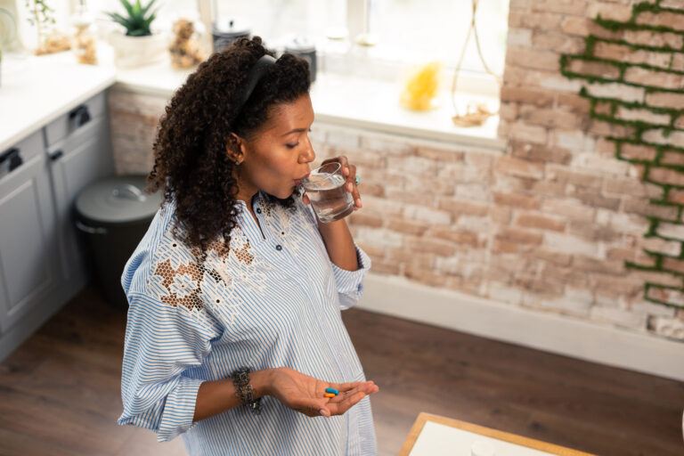 Pregnant lady taking prenatal vitamins with water