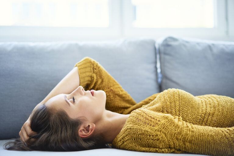 Mom guilt: woman lays on couch with eyes closed