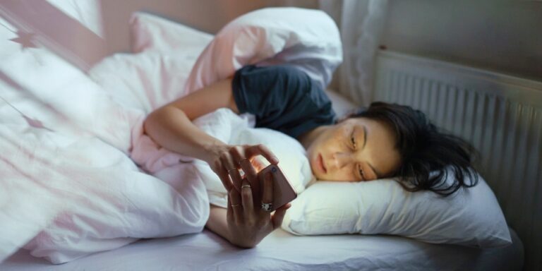 woman laying in bed on her phone - how to stop doomscrolling