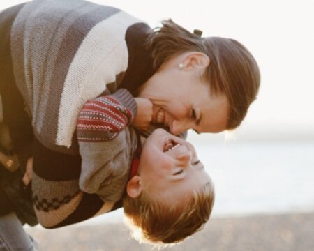 young mom enjoying cuddling with toddler son outside at the beach Motherly