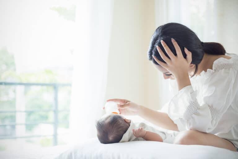 woman feeding baby a bottle on a bed after suffering from a swing of postpartum hormones