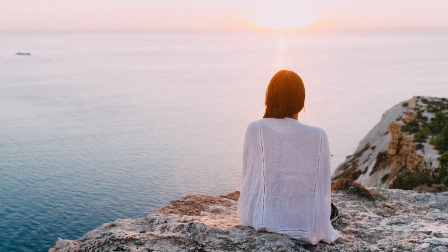 Woman looking out at sunrise over water possibly contemplating the link between miscarriage risk and extreme heat