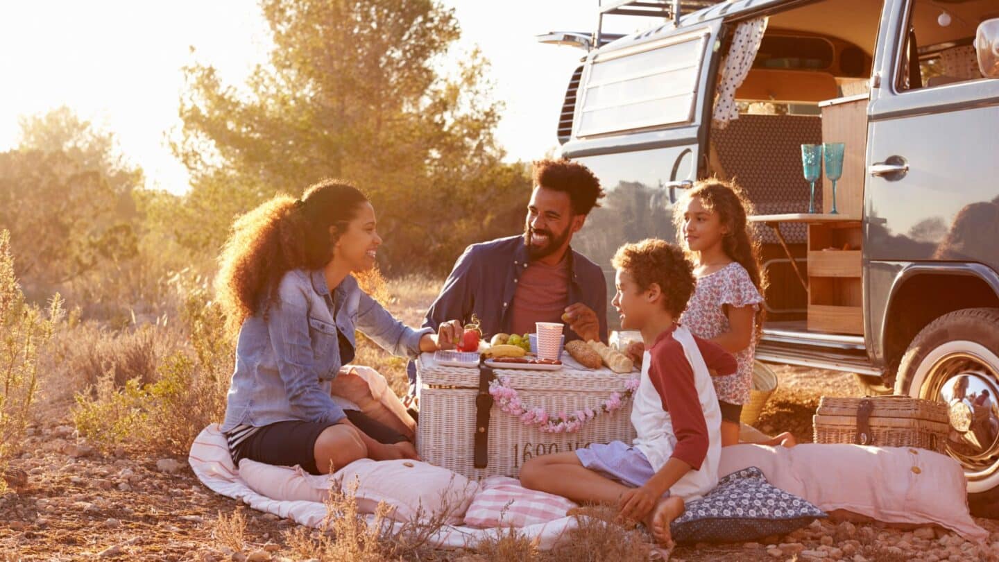 https://www.mother.ly/wp-content/uploads/2022/09/happy-family-eating-outside-car-while-on-road-trip-because-travel-with-kids-boosts-happiness-1440x810.jpg