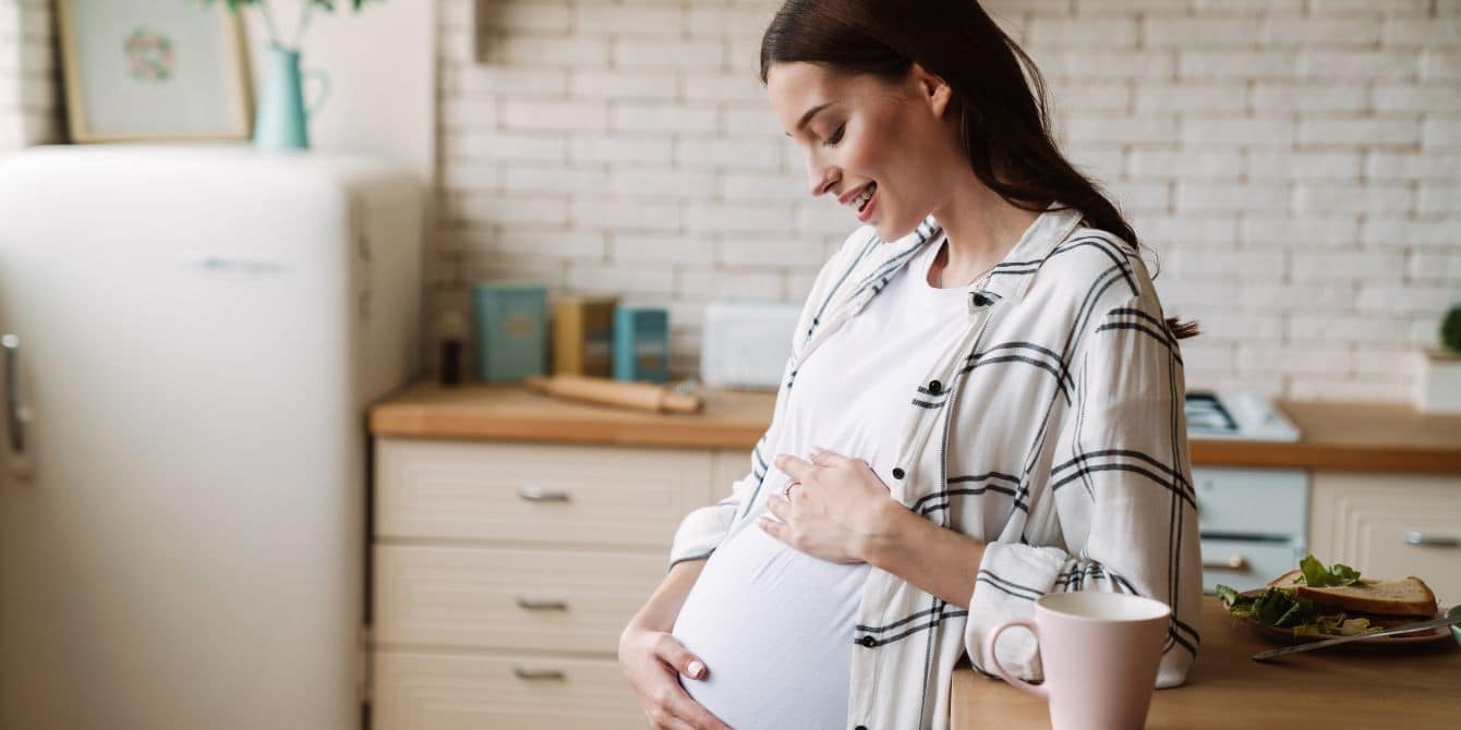 https://www.mother.ly/wp-content/uploads/2022/11/Pregnant-woman-holding-belly-in-kitchen-with-sandwich-on-counter-listeria-outbreak-in-deli-meat-and-cheese.jpg