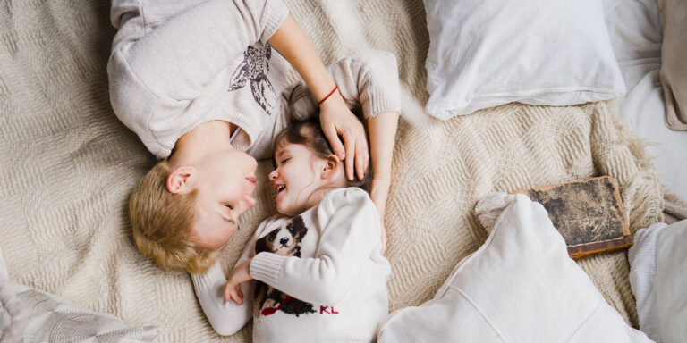 nonbinary parent and daughter hugging in bed