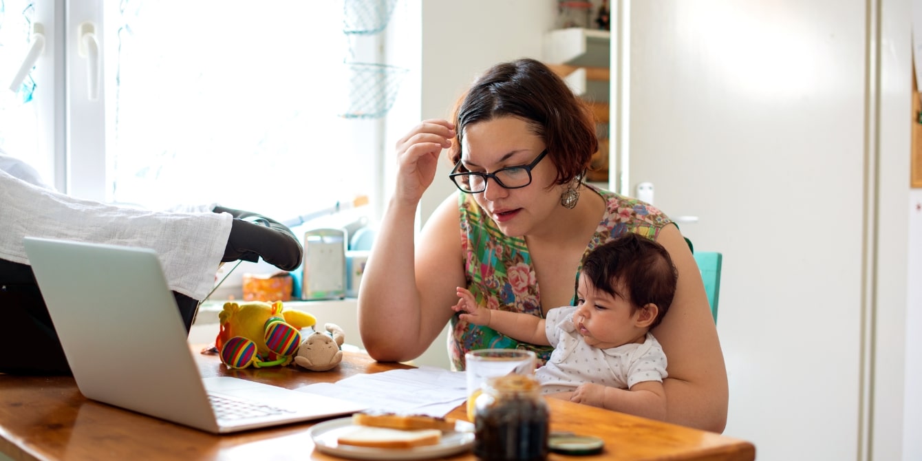 mother holding baby on her lap while working from home -  mental load of motherhood