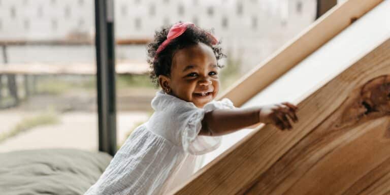 smiling toddler climbing up an indoor slide - 18-month milestones