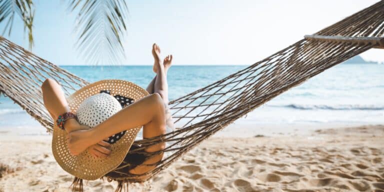 woman wearing sun hat laying on a hammock on the beach- solo getaway