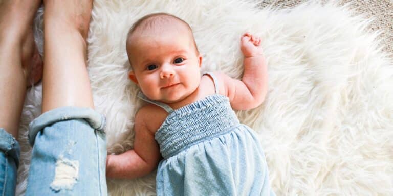 Newborn Baby laying on sheepskin beside moms legs Motherly