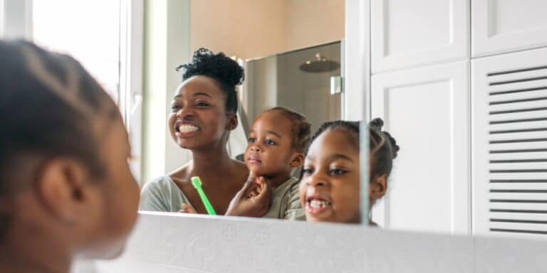 reflection of mom and two children brushing their teeth in a mirror