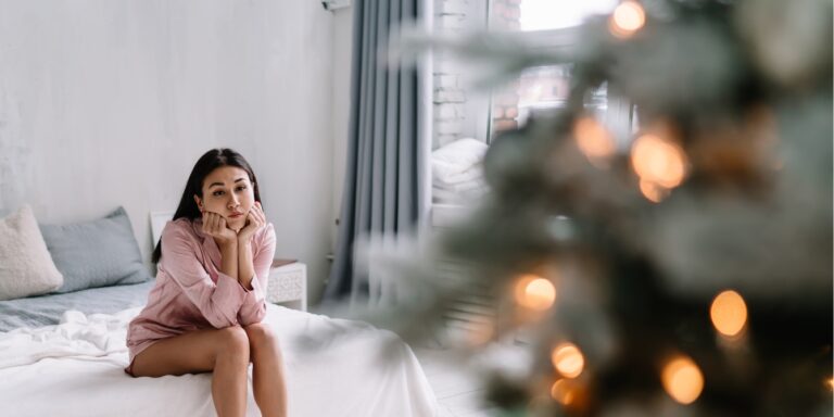 sad woman sitting on bed near Christmas tree infertility and the holidays