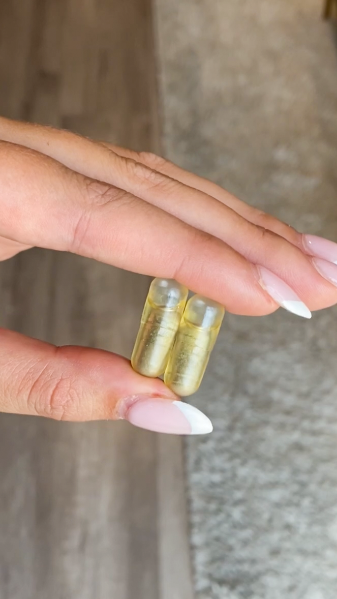 Woman holding two capsules of Ritual Essential for Women Prenatal in hands