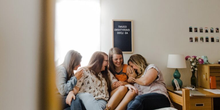 group of women on a couch laughing moms need good friends girls trip