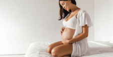 pregnant dark-haired woman wearing a maternity bra sitting on the bed