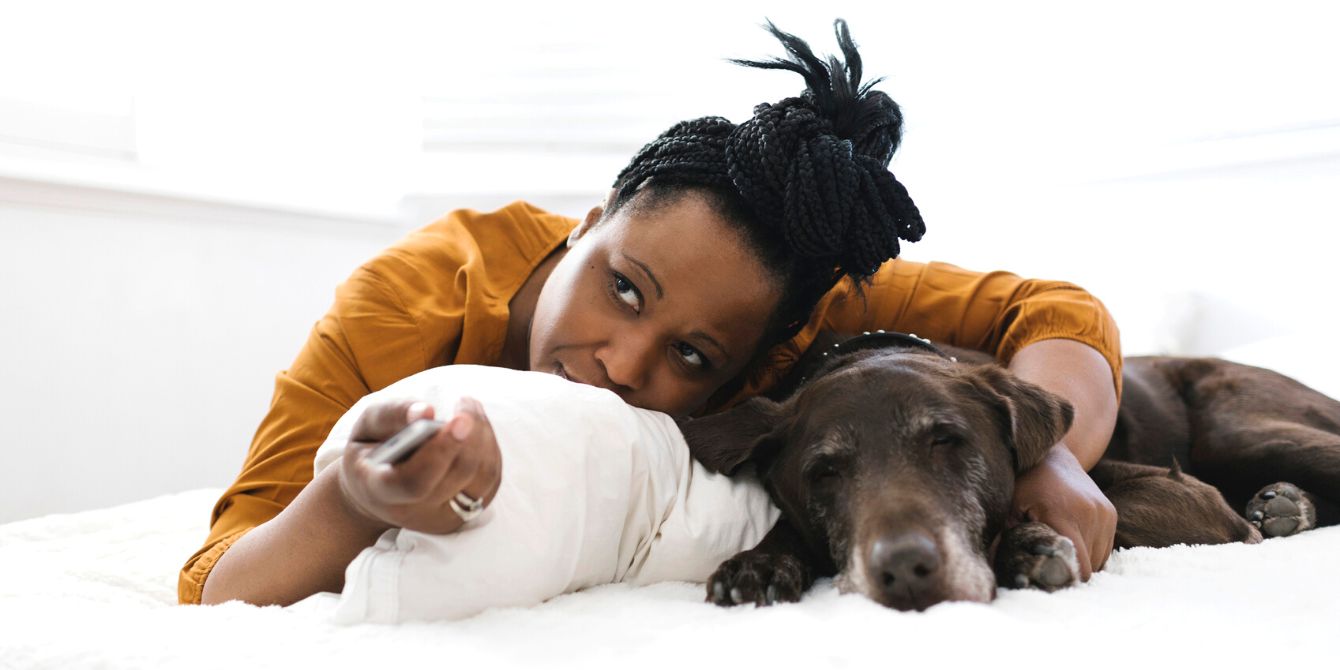 Woman lying in bed with dog watching tv