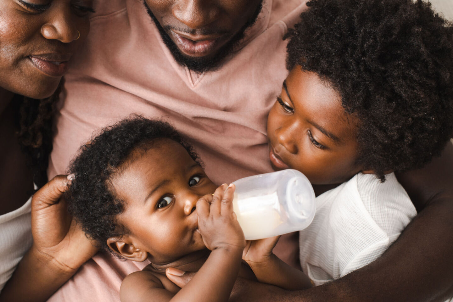 family surrounding baby drinking a bottle