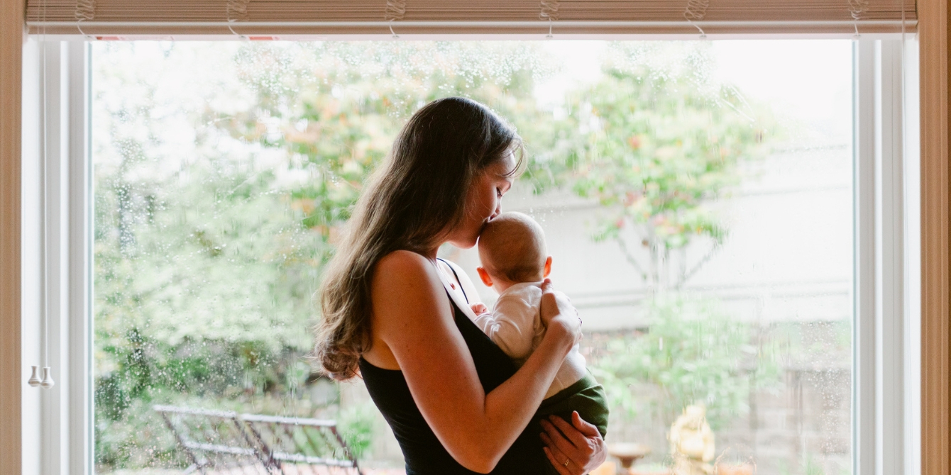 mom kissing baby by window