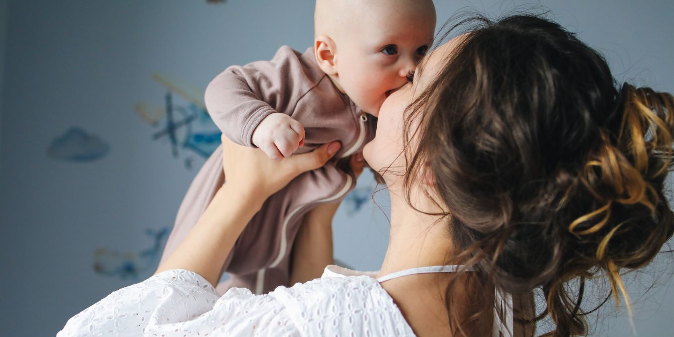 mom holding and kissing baby in the air - using an egg donor