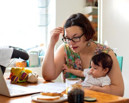 woman holding a baby working from home Motherly