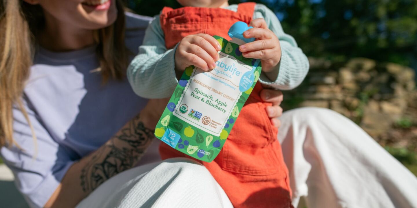 mom holding baby who is holding a Babylife Organics baby food pouch